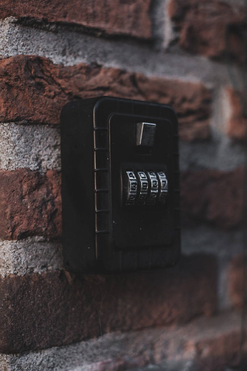 Black combination lockbox mounted on a brick wall.